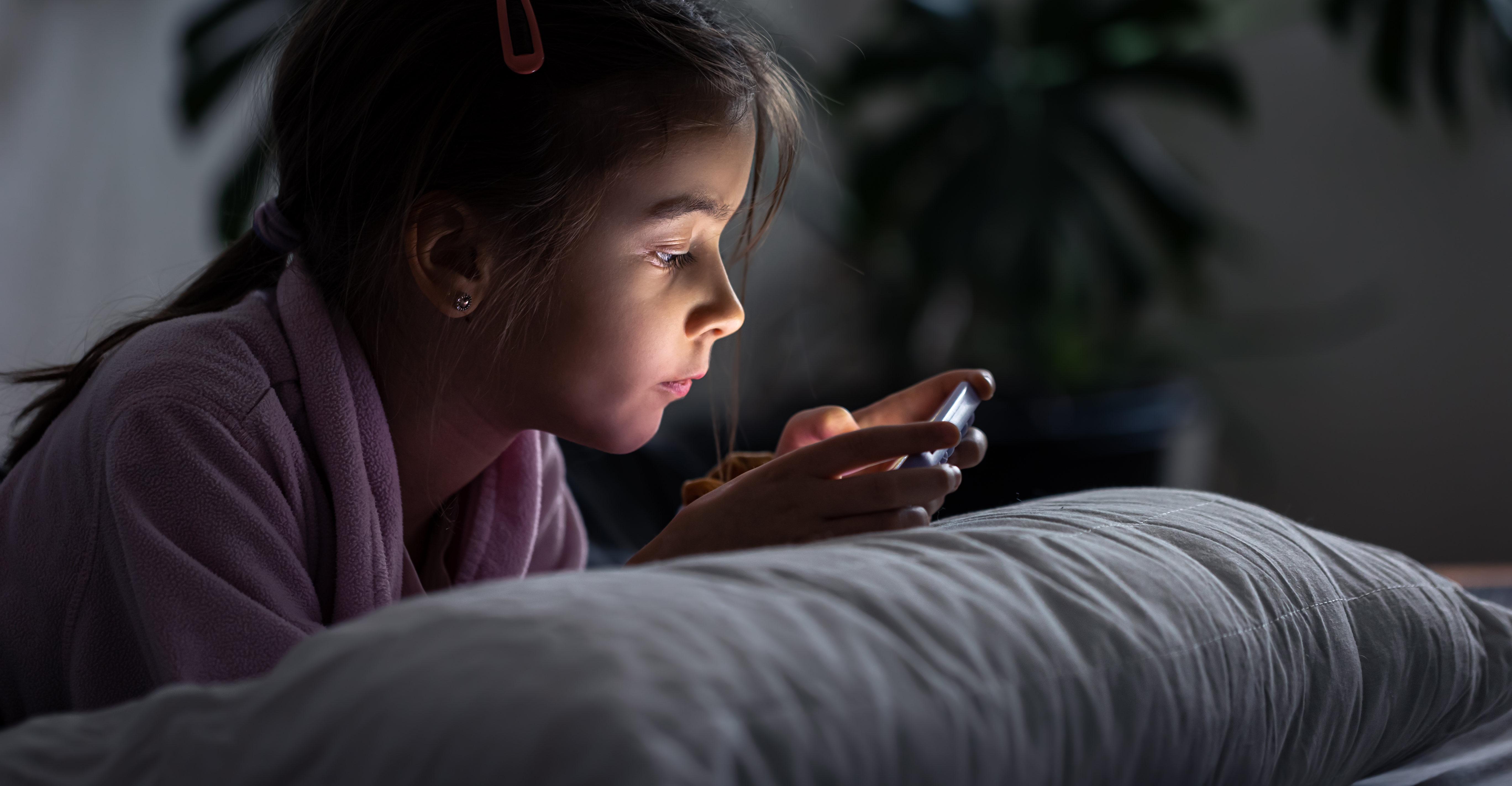 Little girl uses a smartphone lying on the pillow at home.
